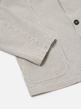 Gros plan sur le tissu texturé seersucker à rayures grises de la Two Button Jacket Grey Derby Stripe Universal Works. Mélange de matières de qualité offrant confort et style. Un équilibre parfait entre structure et souplesse. Venez la découvrir en boutique chez SEE YOU à Versailles.